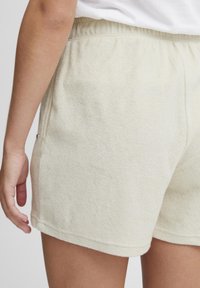 Shorts en éponge beige clair avec une taille élastique et des détails de couture latéraux. Texture douce, coupe décontractée et ourlet simple.