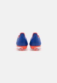 Scarpe da calcio con una tomaia sintetica blu, tallone arancione e suola bianca. Presentano sei tacchetti trasparenti per la trazione su superfici erbose.