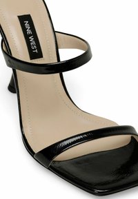 Black patent leather high-heel sandal with two thin straps, square toe, and a textured sole. Labeled "NINE WEST." Light beige interior.