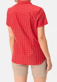 Camicia a maniche corte rossa a quadri con colletto e dettaglio sul dietro, abbinata a pantaloni corti beigi. Il tessuto sembra leggero e strutturato.