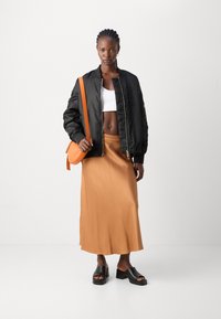 Schwarze Bomberjacke, weißes Crop-Top, brauner Satin-Midi-Rock, orangefarbene Umhängetasche und schwarze Plateau-Sandalen. Glatte Texturen und kräftige Farben.