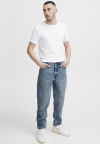 Hvit bomulls-T-skjorte, lyseblå denimjeans med teksturert finish, og hvite joggesko med gullaccenter. Avslappet passform, enkelt design.