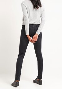 Jeans negros ajustados con una cintura de altura media y bolsillos traseros, combinados con una camiseta gris de manga larga. La tela parece suave con detalles de costura mínimos.