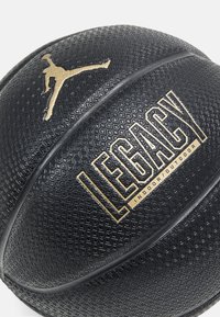 Svart basketball med teksturert overflate, gull "LEGACY"-etikett og Jumpman-logo, designet for innendørs og utendørs bruk.