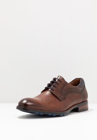 Chaussure en cuir marron à lacets avec une finition lisse, un panneau latéral texturé et des accents de semelle en caoutchouc bleu. Présente des détails de surpiqûre classiques.