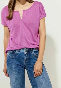 Rosa kortärmad skjorta med V-ringning, tillsammans med ljusblå denimjeans med framfickor och synliga söm detaljer.