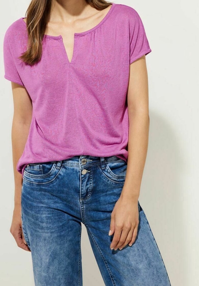 Rosa kortärmad skjorta med V-ringning, tillsammans med ljusblå denimjeans med framfickor och synliga söm detaljer.