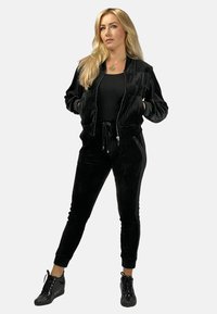 Czarny welurowy dres z zapinaną na zamek bomberką i spodniami na sznurki. Teksturowana tkanina, dopasowany krój, w połączeniu z czarnymi butami sportowymi.
