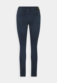 Smala mörkblå jeans med en slät textur, som har två bakfickor och en svart läderlapp vid midjan. Enkelt utseende, inga utsmyckningar.