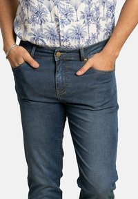 Jeans de mezclilla en un lavado azul oscuro, con un corte slim, diseño de cinco bolsillos, costuras visibles y cierre de botón de metal.