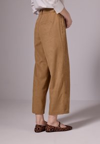 Kamelinsin leveälahkeiset housut korkealla vyötäröllä, sivutaskuilla ja koristeellisilla niiteillä. Musta ja ruskea leopardikuosiset ballerinat täydentävät asun.