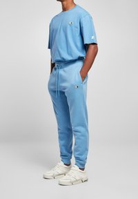 Ljusblå sweatshirt och matchande joggers i mjukt tyg. Vita logotypdetaljer på både tröja och byxor, tillsammans med vita sneakers.