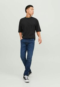Camiseta negra de manga corta, jeans de mezclilla azules y zapatillas negras con acentos blancos; ajuste casual, tejido suave y diseño sencillo.