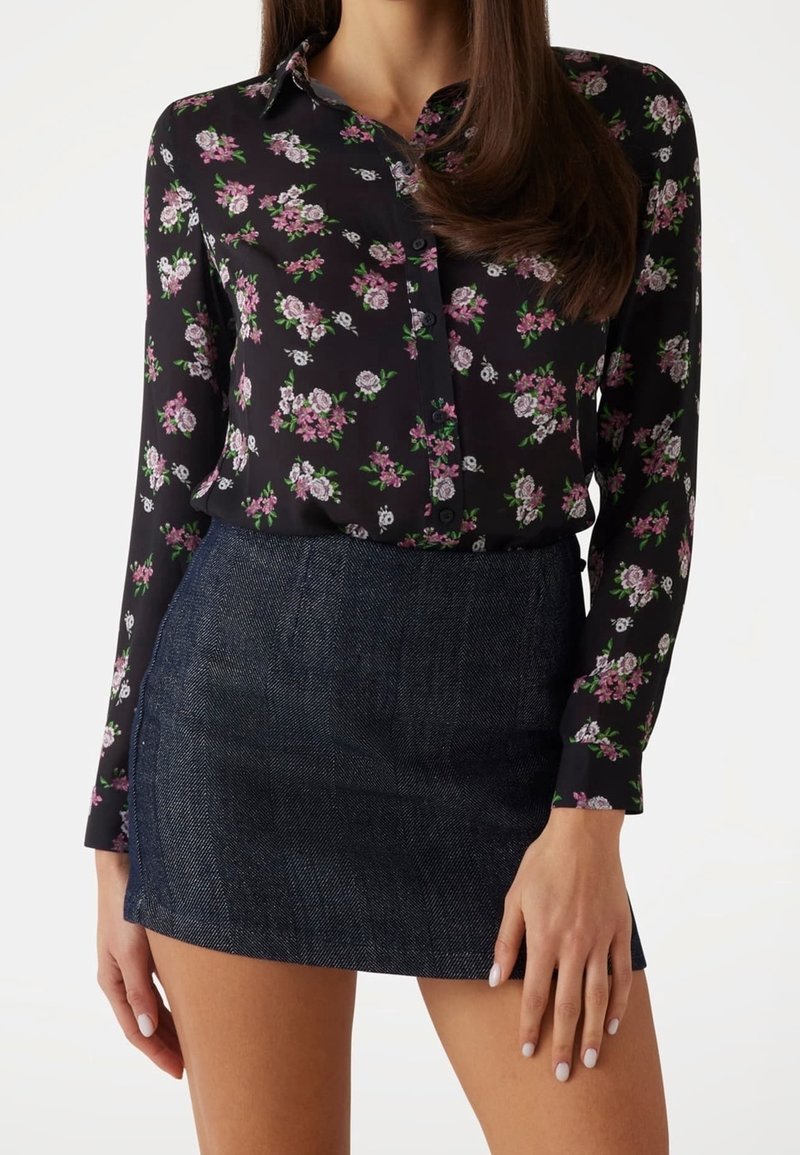 Blouse noire à fleurs avec manches longues et col, ornée de fleurs roses et blanches. Associée à une mini-jupe en denim foncé.
