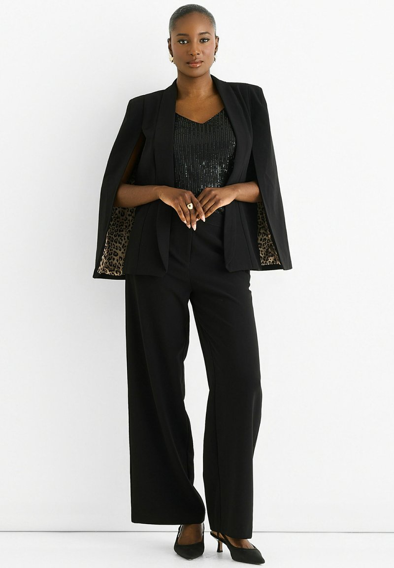 Black tailored suit with a cape design, featuring a sequined top and animal print lining. The outfit is complemented by pointed toe heels.