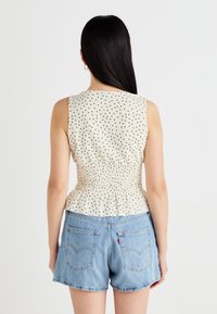 Crème zonder mouwen top met zwarte stippen, gegatherde taille en peplum ontwerp, gecombineerd met lichtblauwe spijkerbroek shorts.