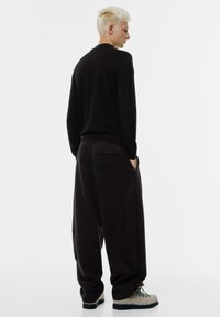 Svart stickad tröja och löst sittande svarta byxor i mjukt tyg. Outfiten har sidofickor och kontrastsömmar på skorna.