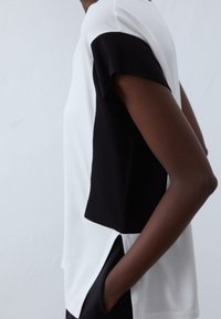 Svart och vit färgblockerad t-shirt med korta ärmar, som har en avslappnad passform och sidofickor för ökad rörelsefrihet och andningsförmåga.