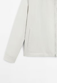 Helle graue Jacke aus glattem Stoff, mit einem Reißverschluss, seitlichen Taschen und einem geraden Schnitt mit sauberen Abschlüssen.