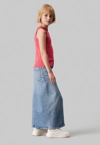 Top sin mangas de color rojo con textura de rayas, combinado con una falda larga de mezclilla azul. El conjunto se completa con zapatillas blancas y cuenta con una abertura lateral.