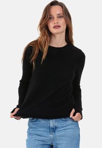 Pull noir côtelé à manches longues et col rond, associé à un jean bleu clair ; tissu texturé avec détails de côtes visibles.