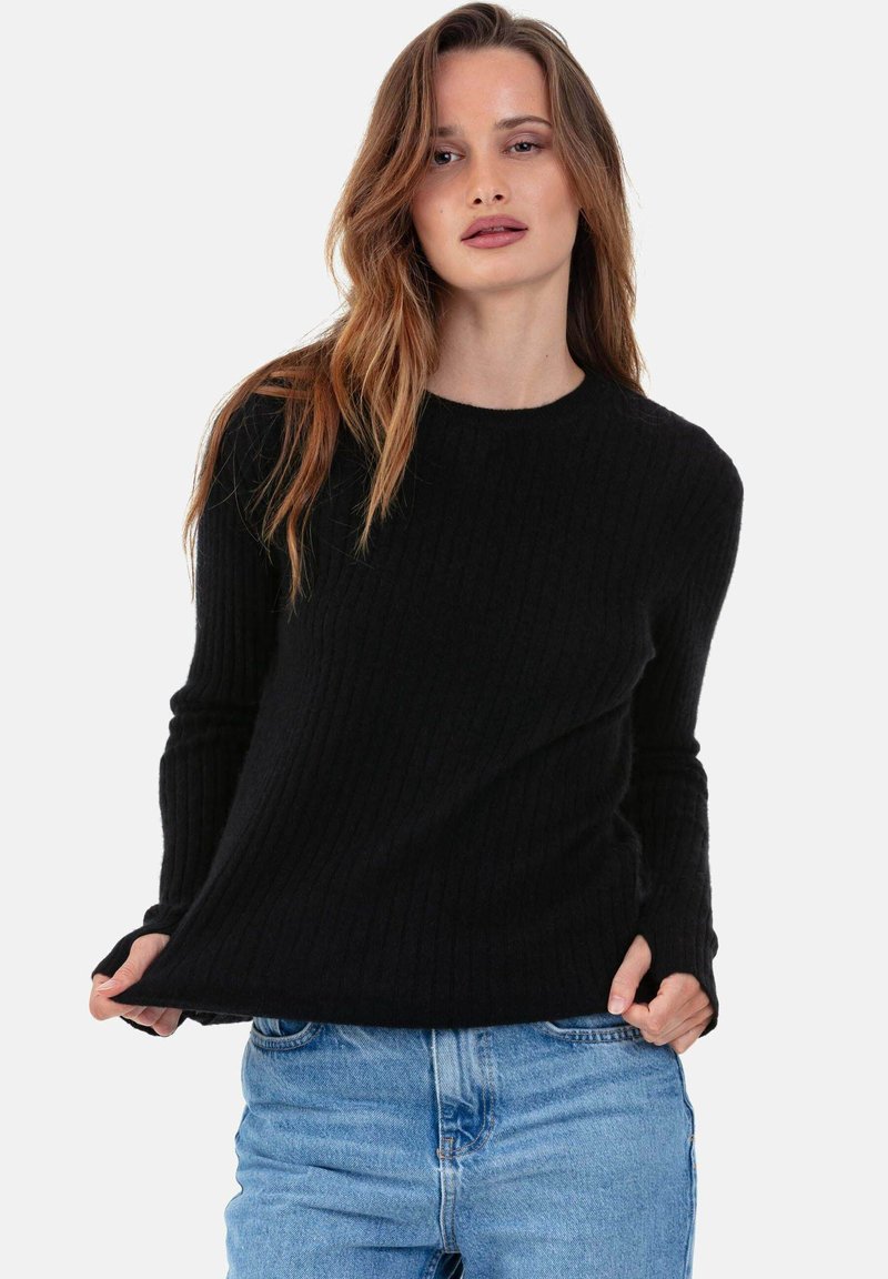 Pull noir côtelé à manches longues et col rond, associé à un jean bleu clair ; tissu texturé avec détails de côtes visibles.