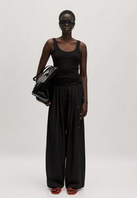 Zwarte geribbelde tanktop en wijde zwarte broek, gecombineerd met rode sandalen. Model draagt een glanzende zwarte handtas en heeft oversized zwarte zonnebril op.