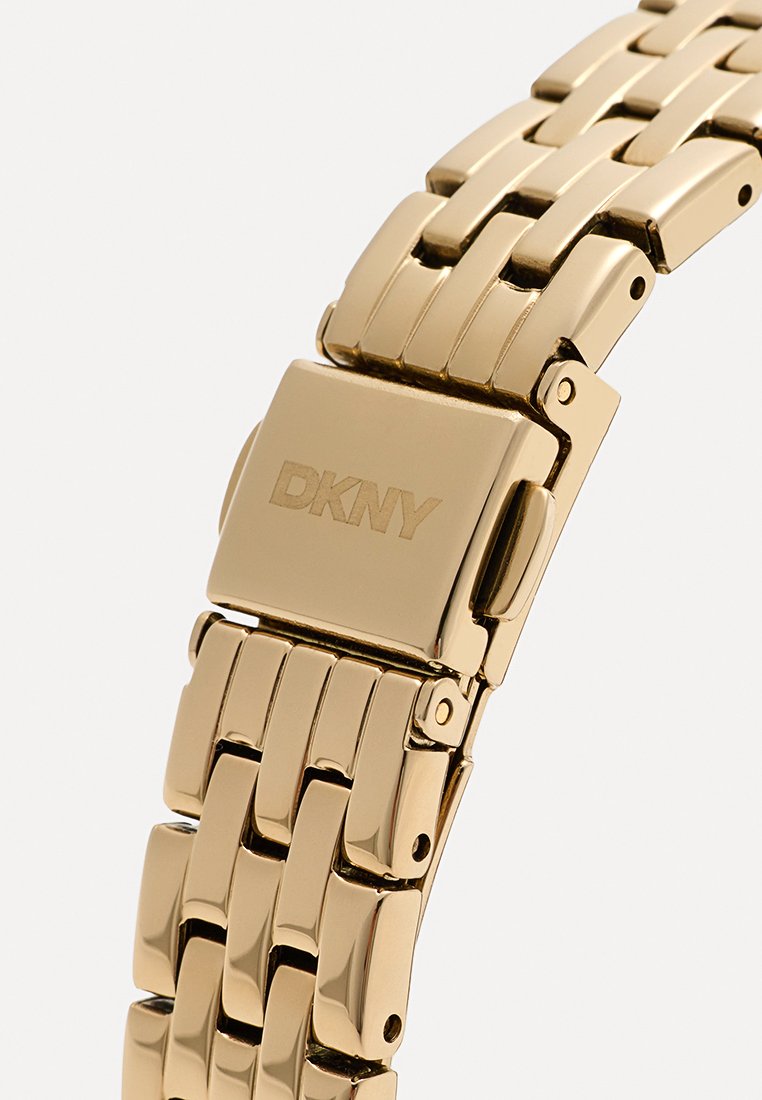 Pulsera de reloj de metal dorado con eslabones entrelazados y acabado pulido. Presenta el logotipo de DKNY en el cierre, textura suave y diseño minimalista.