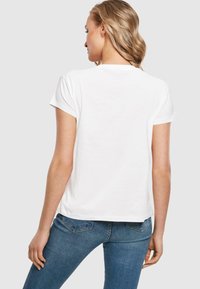 Hvid kortærmet t-shirt set fra ryggen, lavet af glat bomuld. Har en afslappet pasform med en rund halsudskæring. Sammen med blå jeans.