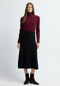 Bordeaux coltrui gecombineerd met een zwarte A-lijn midi rok, voorzien van een brede tailleband en een gestructureerde stof; model draagt bruine enkellaarsjes.