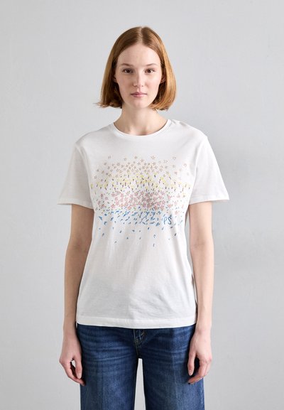 T-shirt en coton blanc avec un design graphique coloré comprenant des motifs floraux jaunes, roses et bleus, à manches courtes et à col rond.