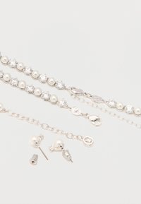 Δύο ασημένια βραχιόλια με εναλλασσόμενες πέρλες και διάφανα πετράδια, κούμπωμα με κλιπ αστακού και ένα ζευγάρι ταυτόσημα σκουλαρίκια με πέρλες.