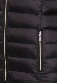 Veste matelassée noire avec des détails en quilt, dotée d'une fermeture éclair argentée et d'accents, texture lisse et motif cousu horizontal.