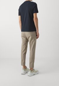 Marineblauw T-shirt met korte mouwen, gecombineerd met lichtbeige afhangende broek; bevat sneakers met een textuur en gelaagd ontwerp in lichtgroen en wit.