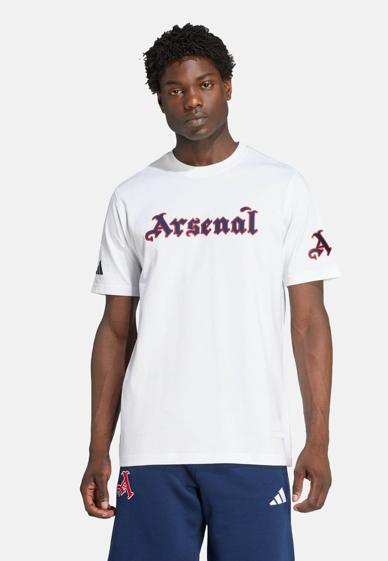 T-shirt blanc à manches courtes avec "Arsenal" en lettres gothiques rouges sur la poitrine et un "A" rouge sur la manche gauche. Matière en coton.