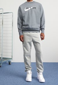 Grå sweatshirt med "AIR"-logotyp, kombinerad med ljusgrå sweatpants och vita sneakers. Slät tyg, avslappnad passform och ribbade ärmslut.