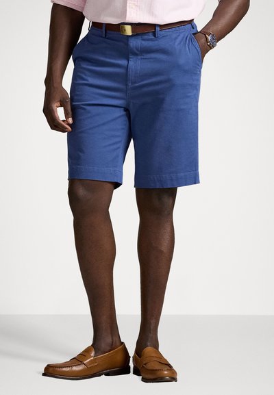 Blå bomulds shorts med flad front, sidelommer og opfoldede kanter. Sammen med brune læder loafers og et brunt bælte.