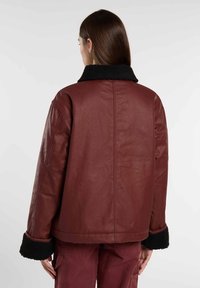 Bordeaux leren jas met een zwarte nepleren kraag en manchet. Heeft een relaxte pasvorm en een gladde textuur. Achterzijde ontwerp met minimale naden.
