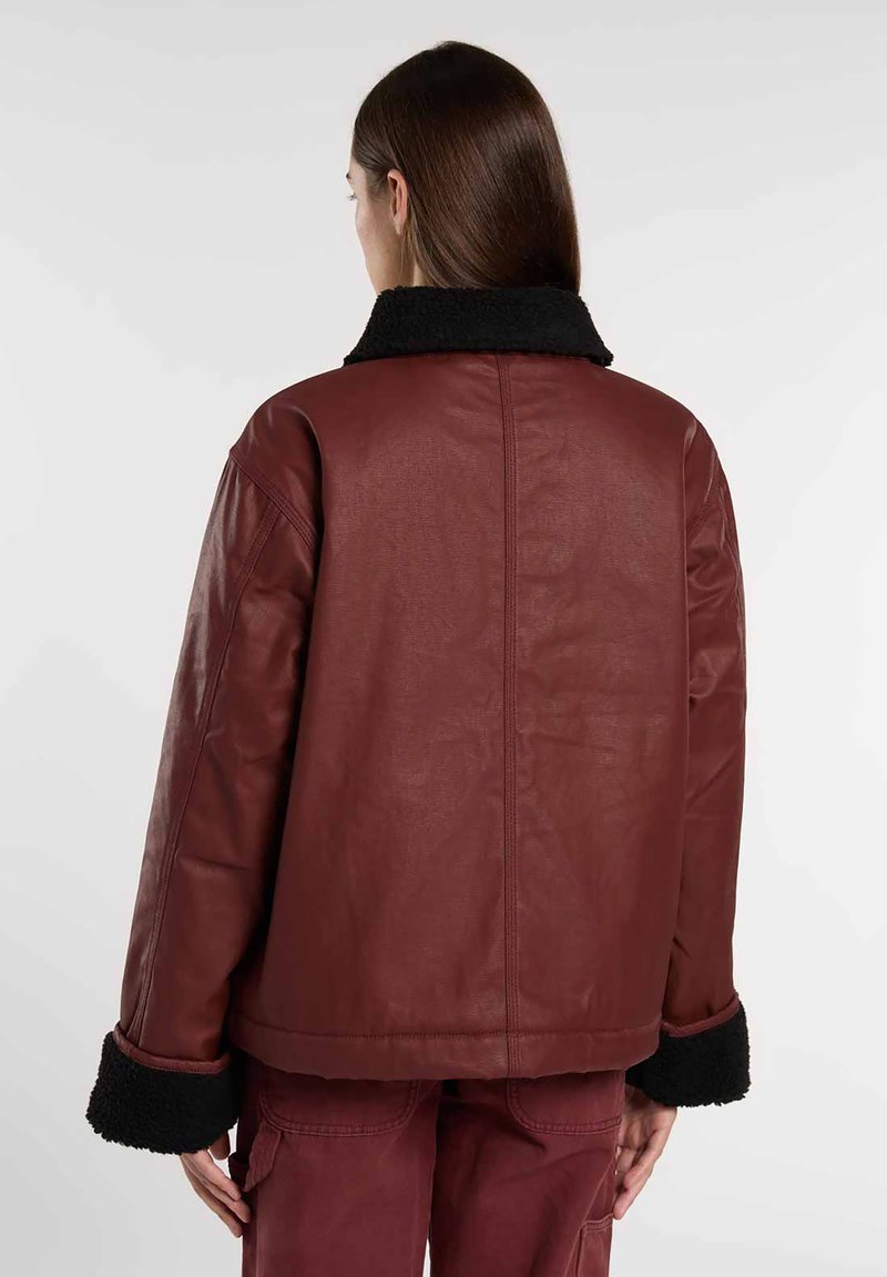 Giacca in pelle bordeaux con collo e polsini in pelliccia sintetica nera. Presenta una vestibilità rilassata e una superficie liscia. Design posteriore con cuciture minimal.