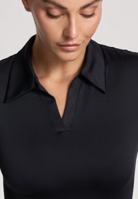 Maglietta polo nera con una texture liscia, caratterizzata da un colletto classico e un taglio a V sottile. Il materiale appare elegante e aderente.