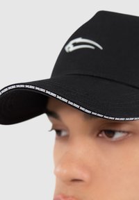 Black cap with a curved brim. Features textured fabric, white branding along the brim, and a logo embroidered on the front.