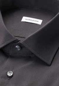Schwarzes Hemd mit spitzem Kragen und zwei sichtbaren Knöpfen, mit einem weißen Etikett mit dem Schriftzug "seidensticker" innen am Kragen.