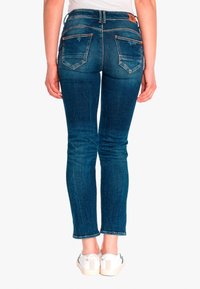 Jeans skinny en denim bleu foncé avec une taille mi-haute, des poches arrière et un léger effet délavé. Associés à des baskets blanches.