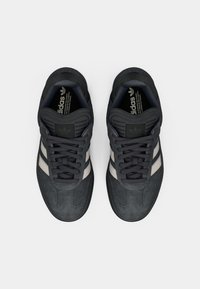 Μαύρα σουέντ αθλητικά παπούτσια με δύο λευκές ρίγες, στρογγυλή μύτη, χοντρές κορδόνια και υφή στη σόλα, με επενδεδυμένο γιακά για υποστήριξη.