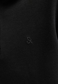 Mustast kangast lähedalt, kus on väike tikitud ampersandi sümbol sobivas mustas niidis.