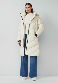 Balta pūkaina jaka ar diognālu šuvju, priekšējo rāvējslēdzēju un kapuci. Kombinēta ar vieglu džemperi un platām ziliem džinsiem. Baltas platformas kurpes.