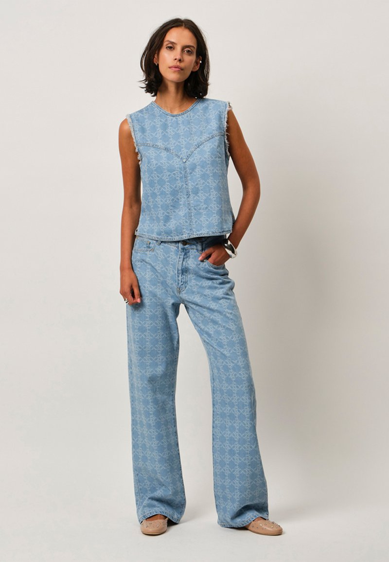 Lichtblauwe denimoutfit bestaande uit een mouwloze cropped top met rafelige randen en brede broekspijpen, beide met een ingewikkeld patroon throughout.