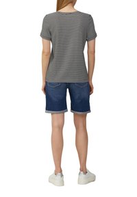 Gestreept zwart-wit T-shirt met korte mouwen, gecombineerd met blauwe denim shorts met opgerolde manchetten en achterzakken, gedragen met witte sneakers.