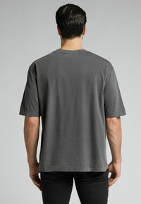 Szara bawełniana koszulka z okrągłym dekoltem i krótkimi rękawami. Tył ma gładką fakturę i minimalne detale szwów.