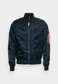 Giacca bomber della marina, materiale in poliestere lucido, chiusura zip, polsini e orlo a costine, tasche laterali e etichetta rossa in tessuto con simbolo di riciclaggio.